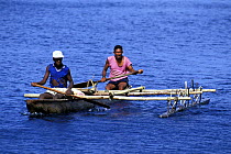 Two men paddling their outrigger through calm blue waters off Ambrym Island, Vanuatu, South Pacific.