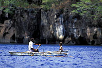 A man and a young boy paddling a small outrigger canoe off the islands of Vanuatu, South Pacific.
