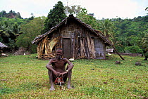 Local man sitting in front of his home in the small village of Matantas, Vanuatu, Pacific Islands. Most houses in the village are made of split bamboo and sago palm leaf roofs
