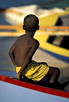 Boy sits on the bow of a wooden dinghy at the Grenada Sailing Festival, Caribbean