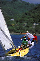 Crew trapezing aboard a traditional workboat during a race off Grande Anse Beach at Grenada Sailing Festival, Caribbean.
