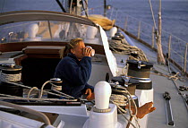 Young woman drinking morning coffee while on watch aboard a cruising yacht from Bermuda to Newport.