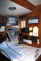 Navigation station aboard a cruising yacht showing instruments, weather fax maps, old sat nav and charts.