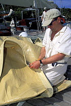 A crew member hand stitching the sails of a superyacht on the dockside during Antigua Classics regatta, Antigua, Caribbean.