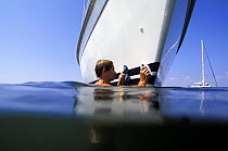 Using a suction handle, the crew of a yacht scrubbing the waterline at anchor.