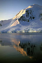 The setting sun on the snow-covered mountains reflecting in the water of the Lemaire Channel, Antarctic Peninsula.