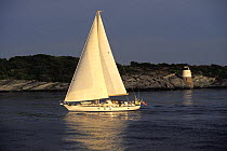 Little Harbor cruising sloop off Castle Hill with lighthouse behind, Newport, Rhode Island, USA.