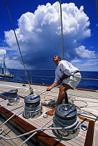 Crew member checking the halyard tension on large sailboat off Antigua, Caribbean, with a rain squall in the background.