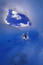 A person standing at the end of a tunnel in a glaciar formed by an ice melt glacial river, Perito Moreno glacier, Los Glaciares National Park, Patagonia, Argentina