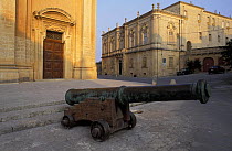 A cannon in front of buildings, Malta
