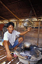 Baju man (sea gypsy) roasting fish over open fire in his house on the southern tip of Walea island, Sulawesi, Indonesia.