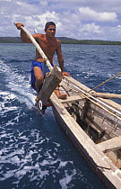 Man on a popow, the traditional outrigger canoe used on Yap, Micronesia. A long pointed paddle is held overboard in the wake of the canoe to act as a rudder.