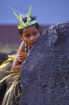 A young Yapese dancer dressed in traditional costume hiding behind a big "rai" (the round stone money that still has value), Yap, Micronesia.