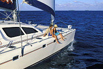 Two people sitting on the edge of a cruising catamaran, Belize.