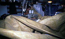 Sailmaker and crew on "The Card". Jim Close, repairs the huge sails down below, 1989-90. ^^^ The boat took part in the Whitbread Round the World Race, 1989-90.