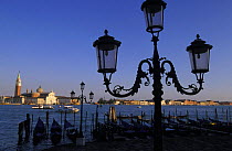 Traditional lamp post and row of gondolas tied to mooring posts with St. Mark's Basilica and the Campanile di San Marco  in the background, Venice, Italy.