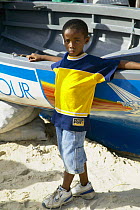 Young local boy standing by a traditional sailing skiff at the Grenada Sailing Festival, Caribbean 2003.