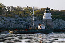 The "Scup" trap fishing boat leaving Newport and Castle Hill Lighthouse in the early morning for the fishing grounds off Newport, Rhode Island, USA