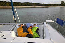 Children asleep at sunrise on the foredeck of a cruising catamaran, Bahamas. Model released.