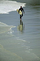 Surfer walking along Black Head Beach, Dunedin, New Zealand.
