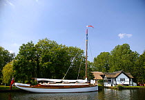 A Broads gaffer moored outside a waterfront house on the Norfolk Broads, England, UK.