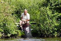 A fisherman patiently waiting for a bite on the banks of the River Bure, Norfolk, UK.