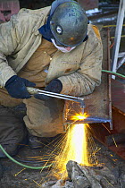 Worker in shipyard cuts metal with acetelene torch