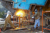 Workers in shipyard cutting metal with acetelene torch.