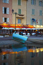 Boat pulled up outside waterside cafes in the port of St Tropez, South France.