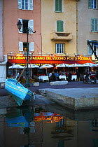 Boat pulled up outside waterside cafes in the port of St Tropez, South France.