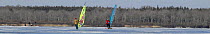 Two people freeskating on Worden Pond, Rhode Island, USA. ^^^ Freeskates are similar to skateboards but with ice blades instead of wheels, and are propelled using a windsurf sail.
