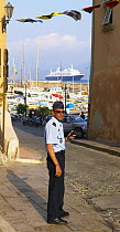 Local policeman in St Tropez, with marina behind, France.