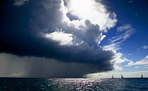 The fleet of small workboats racing in the Grenada Sailing Festival with a heavy squall overhead, Grenada, Caribbean.