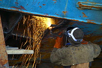 Worker in shipyard cutting metal with acetelene torch.
