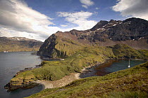 The coastline of South Georgia with a cruising yacht anchored in the sheltered Cobber's Cove to the right.