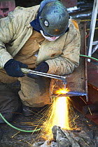 Worker in shipyard cutting metal with acetelene torch.