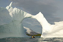 The crew of yacht "Shaman" in the yacht's tender, heading through a natural arch in an iceberg, south coast of South Georgia.