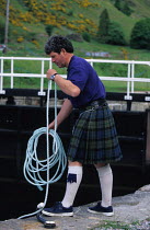 Scotsman in kilt preparing to throw a line to boats in the lock at Laggan during the Great Glen Raid, Scotland. ^^^Rowing in the narrow stretches and sailing through the lochs, the Great Glen Raid com...