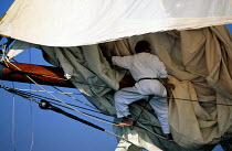 Crew member on William Fife schooner "Altair" lashing a foresail on her bowsprit.