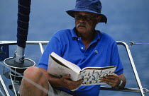 Man reading a book in the pulpit of a sailing yacht. Jean Mauviel is a yachting writer and lawyer, a distinguished member of the Yacht Club de France.