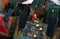 Repairing fishing nets aboard a trawler moored in St Guenole harbour, South Finistere, Brittany, France.
