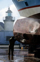 Man pressure washing the hull of a trawler before a coat of anti-fouling is applied. Guilvinec- Lechiagat, South Brittany, France.