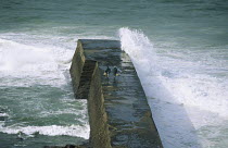 Two men fishing from the stormy jetty in Saint Jean de Luz, Pyrénées Atlantiques, France.
