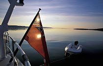 The midnight sun glowing through a flag on a cruising yacht towing a tender in Spitsbergen, Svalbard, Norway, 1998. Property Released.