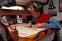 Man navigating with chart and parallel rule on a table in the cabin of a yacht.