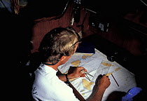 Man with dividers doing chartwork in cabin aboard a yacht.