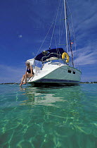 Woman sat on the stern of a cruising yachts dangling her toes in the water, Bahamas.