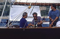 Eric Tabarly at the helm of the original "Pen Duick" at the start of a regatta in South of France. He is more interested by the Chateauneuf du Pape bottle (his favourite wine) than by the timing of th...