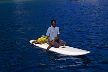 A local man on a paddle board with bananas and other fruit to sell to visiting yachts, Caribbean.