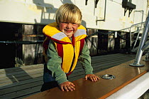 Young boy in a buoyancy aid at a marina. Model released.